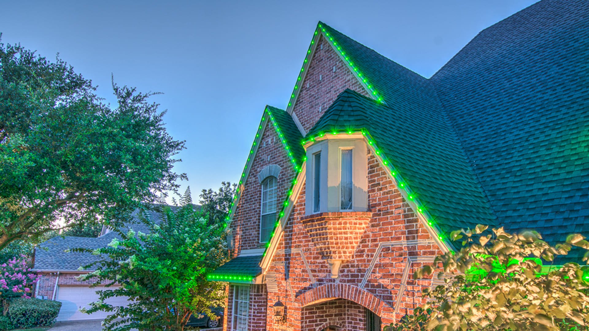 Green and blue permanent lighting highlighting a home’s roof peaks