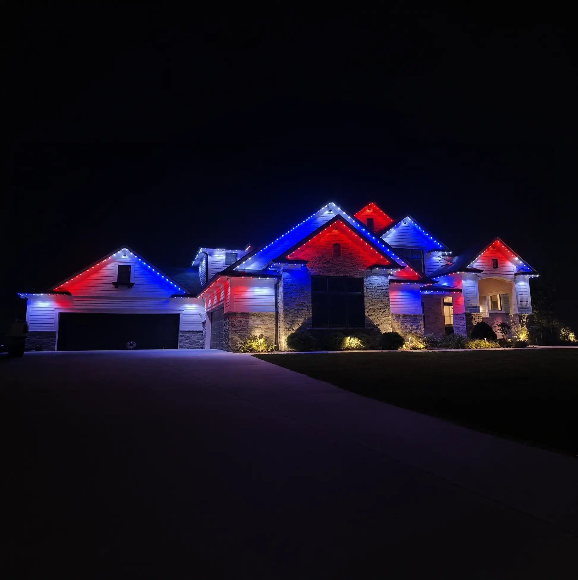 Permanent roofline lighting displaying red, white and blue colors on a home